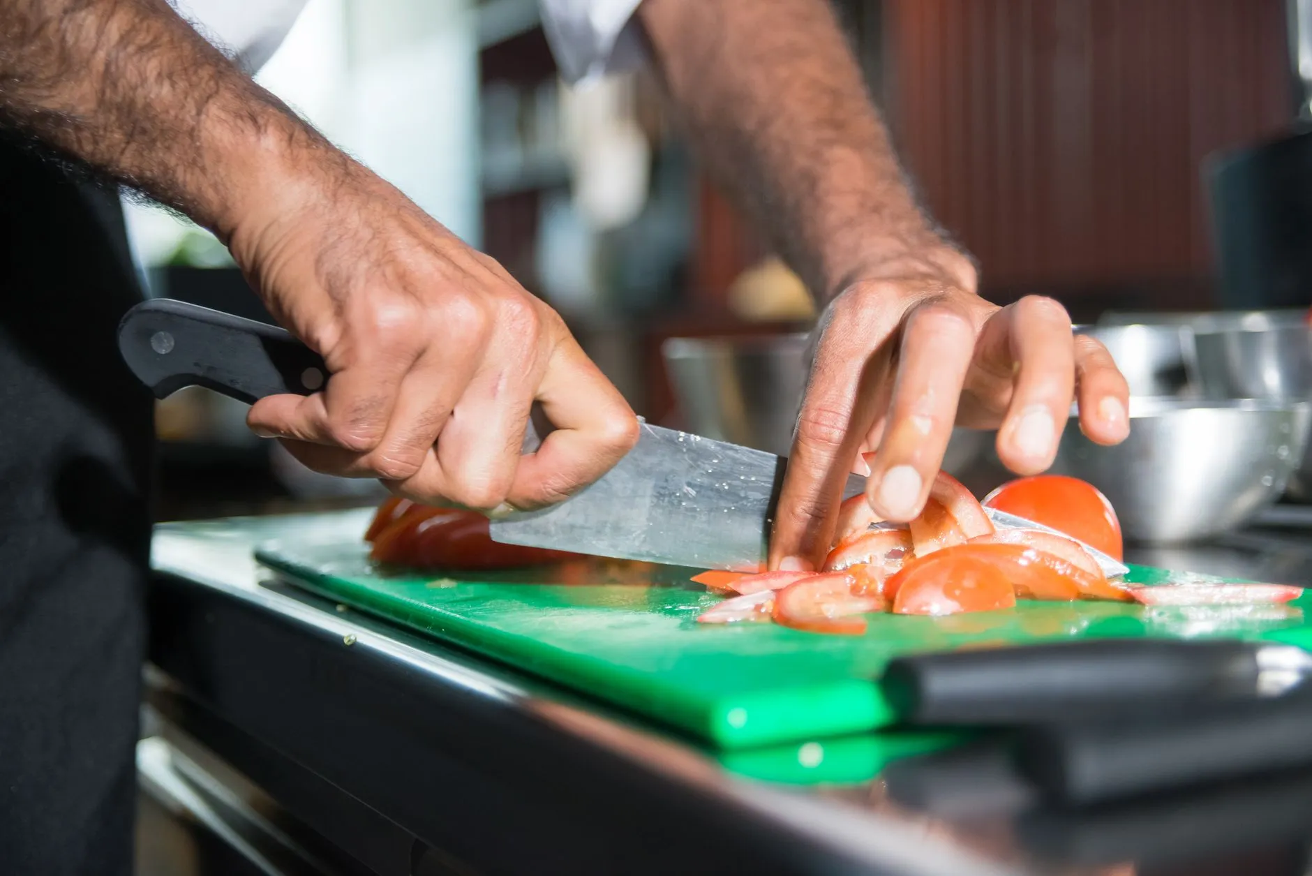 Close-up of a chef slicing fresh tomatoes on a green cutting board in a modern kitchen.