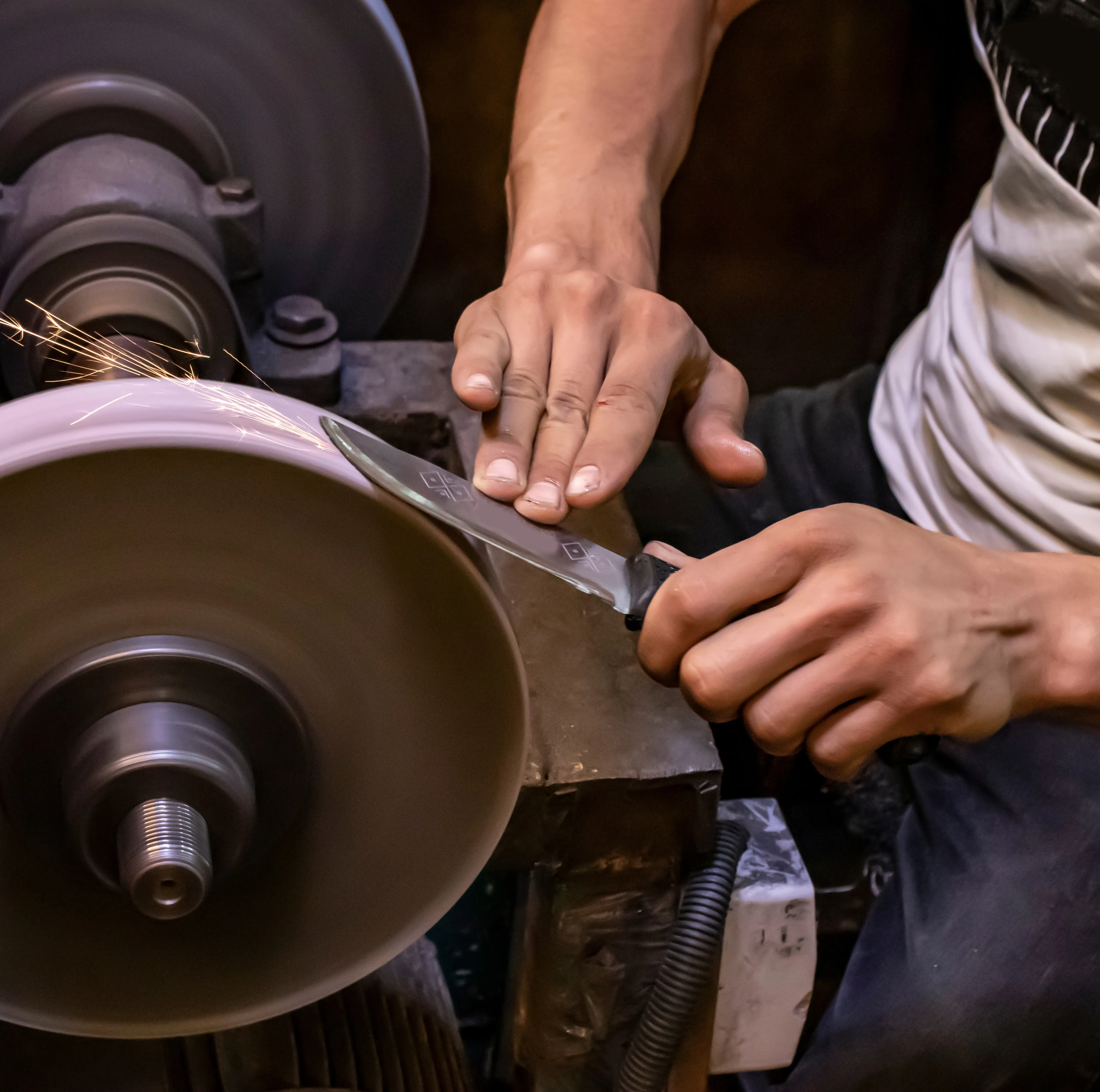 Hands re-profiling a knife edge on a grinding wheel, sparks flying